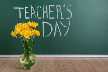 Vase of beautiful flowers on wooden table near blackboard with text TEACHER'S DAY in classroom