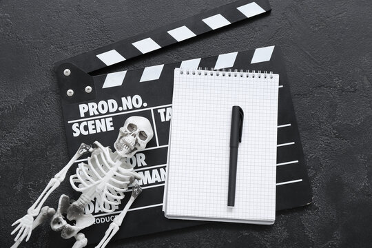 Clapperboard with notebook and skeleton on grunge black background. Halloween celebration