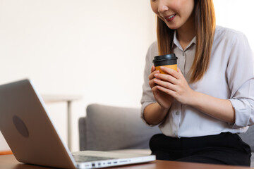 Asian woman drinking a hot coffee in the morning while working with a laptop
