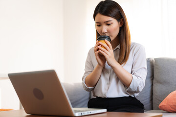 Asian woman drinking a hot coffee in the morning while working with a laptop