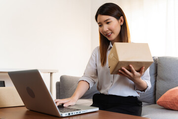 Online seller. Asian woman is packing the cardboard boxes at home
