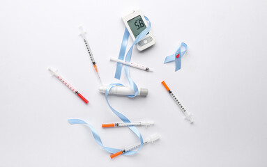 Glucometer with awareness ribbon, lancet pen and syringes on white background. Diabetes concept