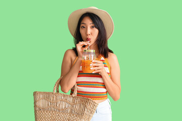 Beautiful Asian woman drinking juice on green background