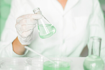 Within the lab: Aide performs tasks within the laboratory environment. Wearing a lab coat. Green hues prevalent. Utilizing glass apparatus. Engaged in plant research in the green laboratory.