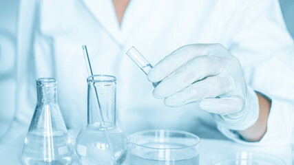 Lab backdrop: Lab assistant carries out manipulations in the laboratory atmosphere. Adorned in a lab coat. Using glass instruments. Located in a blue laboratory. Working with transparent liquid.