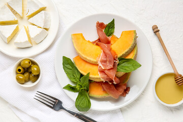 Composition with plate of tasty melon, prosciutto, cheese and olives on light background