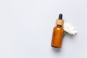 Bottle of essential oil with chamomile flower on light background