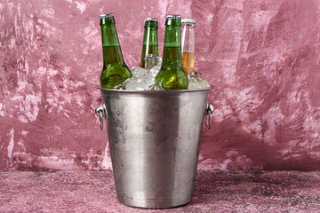 Bucket with bottles of cold beer and ice cubes on purple background