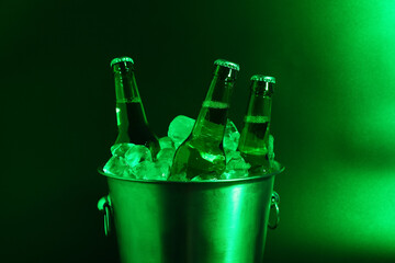 Bucket with bottles of cold beer and ice cubes on color background