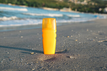 Bottle of sunscreen cream on sand near ocean at beach