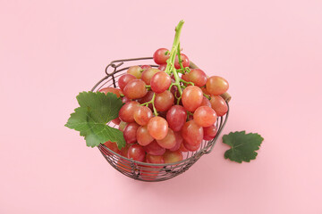 Basket with tasty ripe grapes on pink background