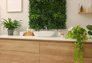 Green artificial plants, vanity and different personal care products in bathroom