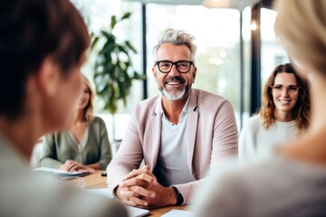Smiling mature businessman in eyeglasses looking at camera during meeting with colleagues in office