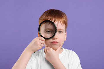Thoughtful boy looking through magnifier glass on violet background