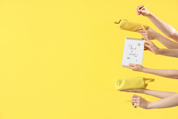 Many female hands holding different stationery and notebook with text BACK TO SCHOOL on yellow...