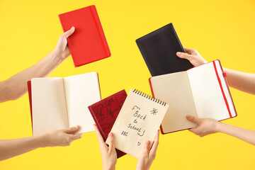 Many female hands holding notebooks with text BACK TO SCHOOL on yellow background