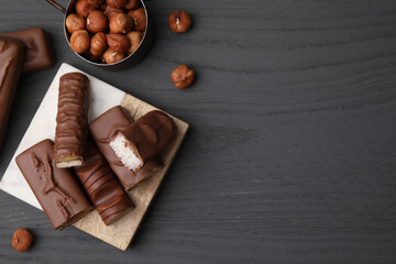 Pieces of different tasty chocolate bars and hazelnuts on grey wooden table, flat lay. Space for text