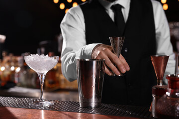 Bartender preparing fresh alcoholic cocktail in martini glass at bar counter, closeup