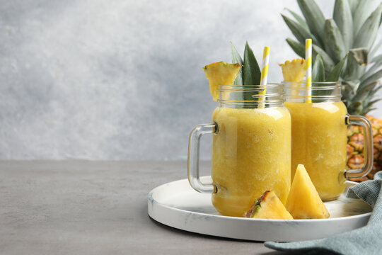Tasty pineapple smoothie and sliced fruit on grey table. Space for text