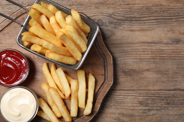 Fototapeta na wymiar Tasty French fries served with sauces on wooden table, top view. Space for text