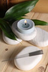 Stones with acupuncture needles and burning candle on wooden table