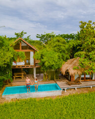 a couple of men and women in front of a Bamboo hut homestay farm, with Green rice paddy fields in Central Thailand with a small plunge pool