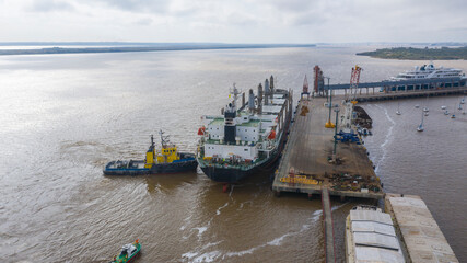 Self unloading bulk carrier arriving in South American port. Assisted by tug boat. Aerial stern view.