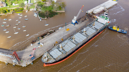 Self unloading bulk carrier arriving in South American port. Assisted by tug boat. Aerial top down view.