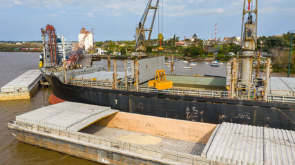 Fototapeta na wymiar Self unloading bulk carrier cargo hatches open unloading sugar. Sugar is loaded onto barges and trucks. Aerial close up view of grab bucket.
