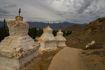 Many white Stupas in a row on a mountain with clouds and blue sky in the background
