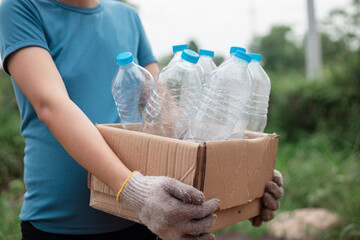 Plastic bottle in paper box. Woman sorting garbage, holding carton box full of plastic bottles for preserving saving environment nature protection. - obrazy, fototapety, plakaty