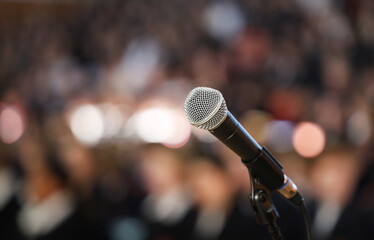 Close up of a microphone on stage with a burred bokeh audience or crowd. Public speaking performing...
