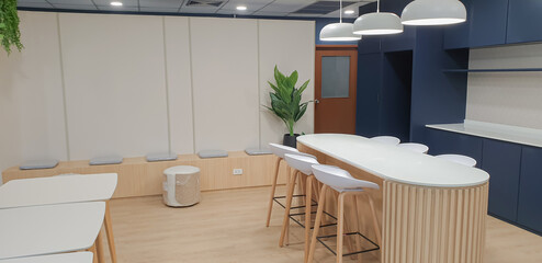 Interior photography of a modern office breakout area with kitchen, blue and grey cabinets, orange pendant lights, polished concrete floors, hanging plant baskets, tables and chairs