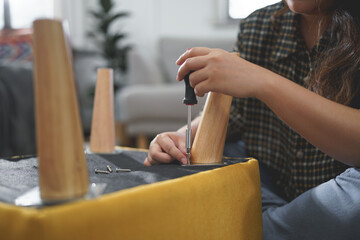 Women use screwdriver equipment to tighten screw while assembling leg of chair to making furniture
