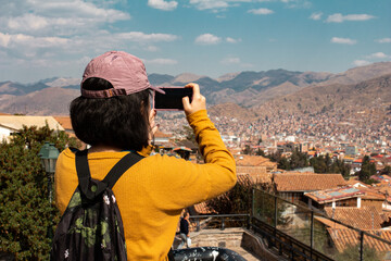 Turista con celular en la mano tomando fotografías la ciudad de Cusco desde el Mirador de San Blas en los Andes peruanos