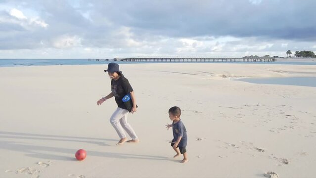 A mother is playing ball with her child on a wide and beautiful sandy beach on a sunny day.