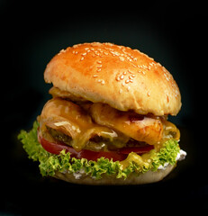 Close-up of a delicious fresh homemade burger with lettuce, cheese, onion and tomato on a rustic wooden board on a dark background