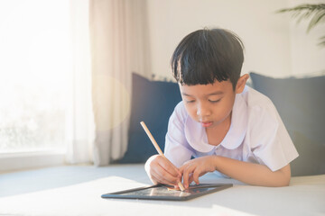 Happy Asian boy 6-7 years old, black hair, white skin, wearing white shirt and blue shorts writing on a chalkboard. Children in school uniforms of Thailand. concept about education, play, creativity.