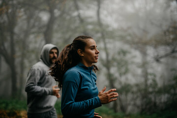 Two runners tackling an uphill path enveloped in fog, symbolizing challenges and determination.
