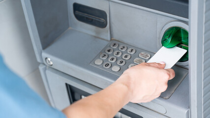 A faceless woman inserts a credit card into an ATM. Close-up of a woman's hands using an ATM machine.