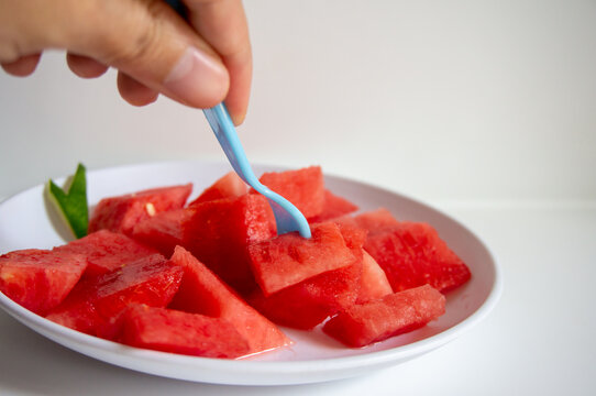 Fresh watermelon ready to eat using a blue fork on a white plate with a white background