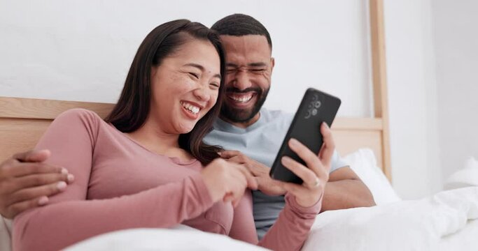 Bedroom, cellphone and happy couple laugh, relax and reading funny communication, meme website or web comic. Smartphone, morning and Asian woman, man or diversity people streaming comedy video on bed