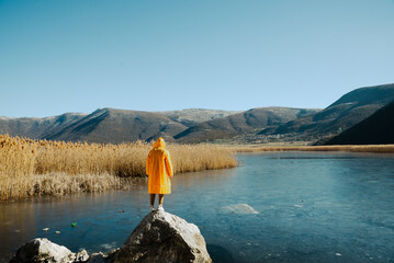 A Person in a Yellow Raincoat Overlooking a Lake and Mountains