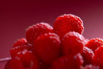 Micro close up of raspberries in glass bowl with copy space on red background