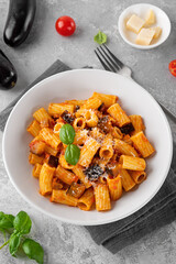 Pasta alla Norma. Italian pasta with eggplant, tomato sauce, cheese and basil in a gray concrete background. Comfort food.