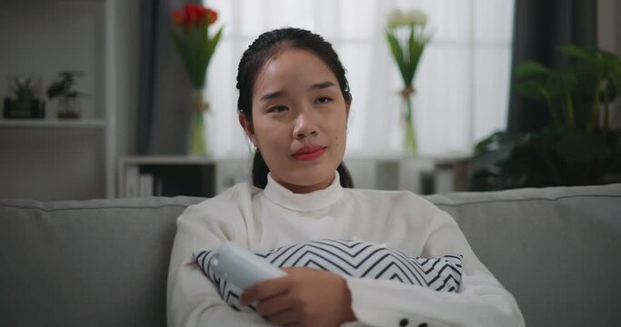 Footage of Happy young Asian woman watching a movie on television while sitting on the sofa in the living room. Wellness at home, relaxing and lifestyle concepts.