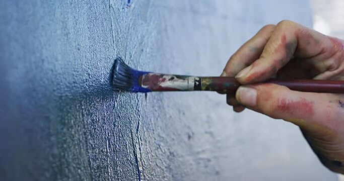 Hand of biracial female artist painting on canvas in art studio, slow motion