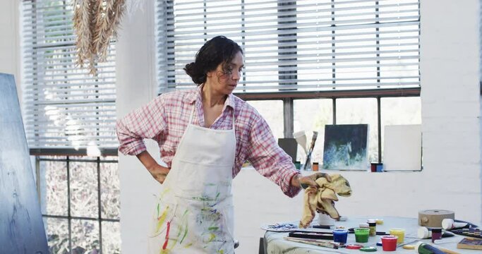 Biracial female artist in apron in art studio, slow motion