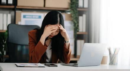 Asian woman feeling migraine head strain.Overworked businesswoman financier while working on laptop and tablet at office.