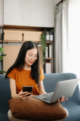 Female students note from the books at the Asian girl library sitting at the sofa using laptop computer and tablet to search an online informations.